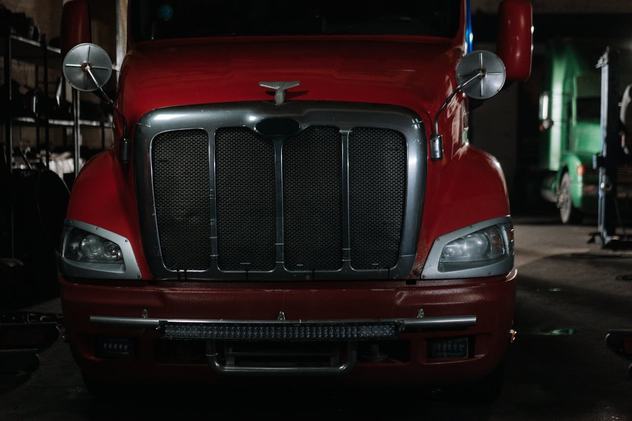 Close-up of a classic red semi truck in a dimly lit garage with chrome details.